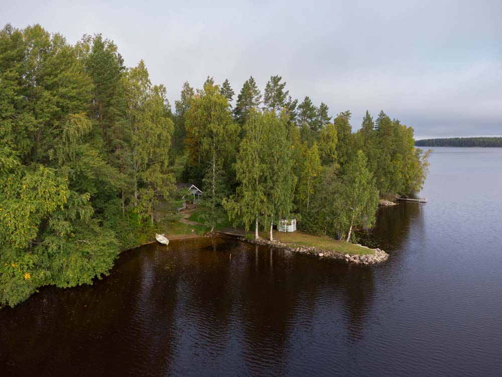 Ilmakuva Kannonjärven metsäisestä rannasta, jossa näkyy pieni laituri ja soutuvene.