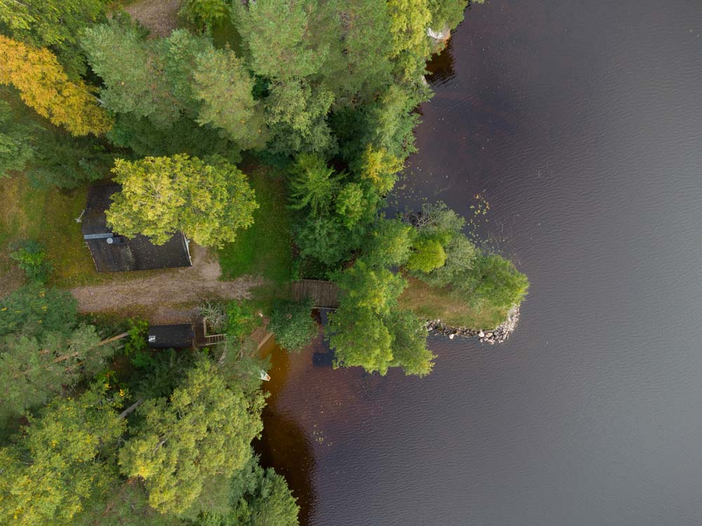 Hiekkarannan mökkipiha Kannonjärven rannalla ilmasta kuvattuna, metsän ja veden ympäröimänä.