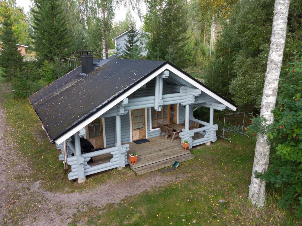 Sini-mökki ylhäältä kuvattuna metsäisessä pihapiirissä, jossa on terassi ja puinen pöytäryhmä.