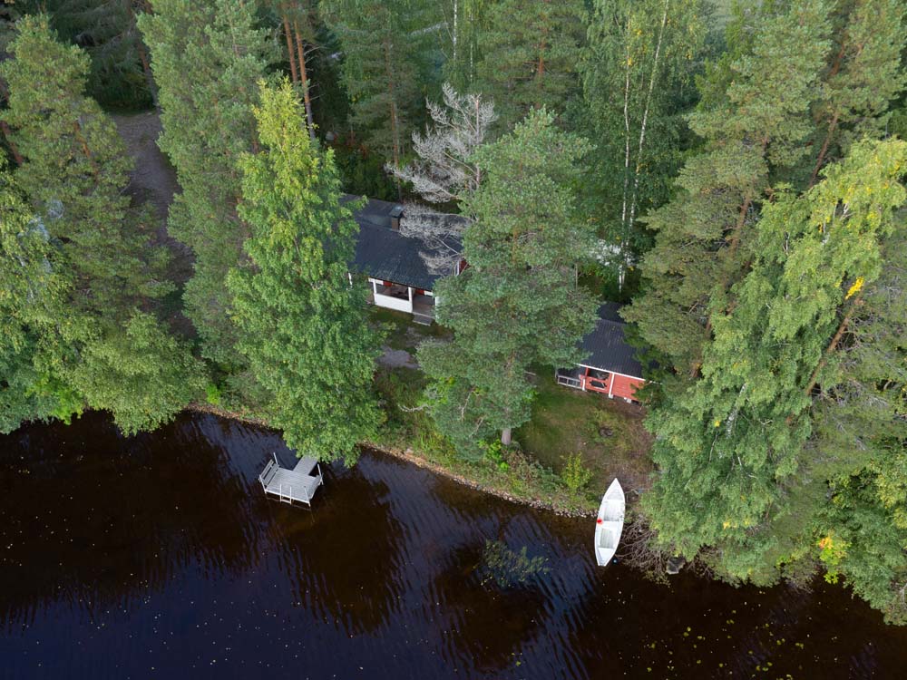 Metsäinen järvenrantamaisema, jossa Mikkilä-mökki, laituri ja soutuvene näkyvät Kannonjärven rannalla.