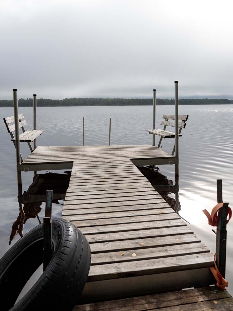 Puurakenteinen laituri tyynellä Kannonjärvellä, reunalla penkit ja etualalla veneen keula.