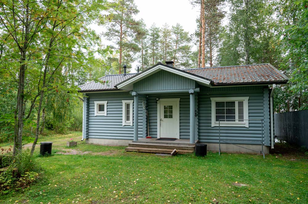 Kulmala-mökki metsän keskellä nurmipihoineen ja pienine terasseineen.