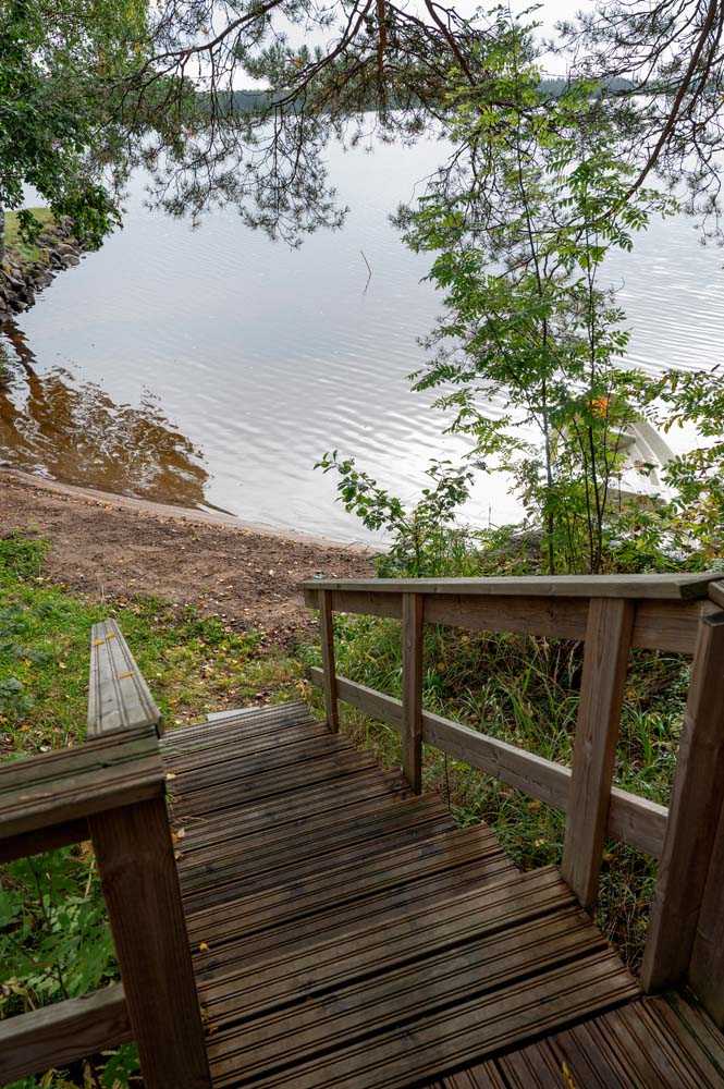 Mökin puuterassilta avautuu näkymä Kannonjärven hiekkarannalle ja tyynelle järvelle puiden kehystämänä.