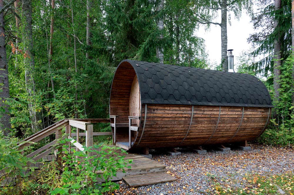 Hirsinen tynnyrisauna metsässä puisten portaiden vieressä.