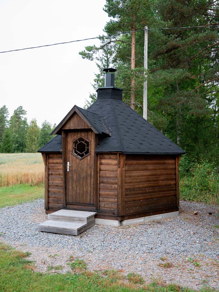Pieni puinen grillikota sorapihalla metsän reunassa.