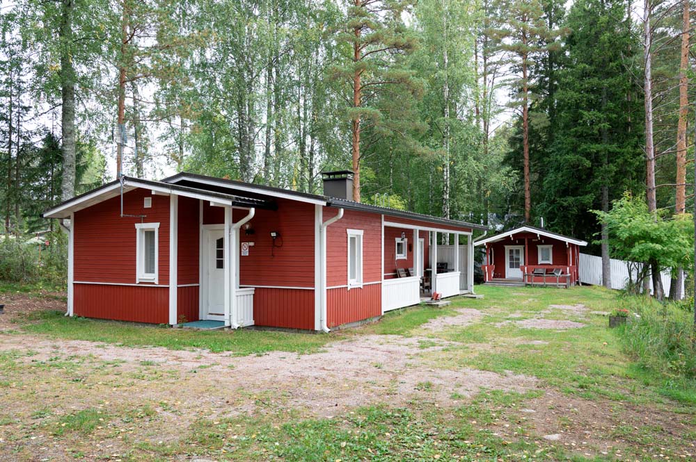 Punainen lomamökki metsäisessä pihapiirissä, taustalla pieni punainen piharakennus.